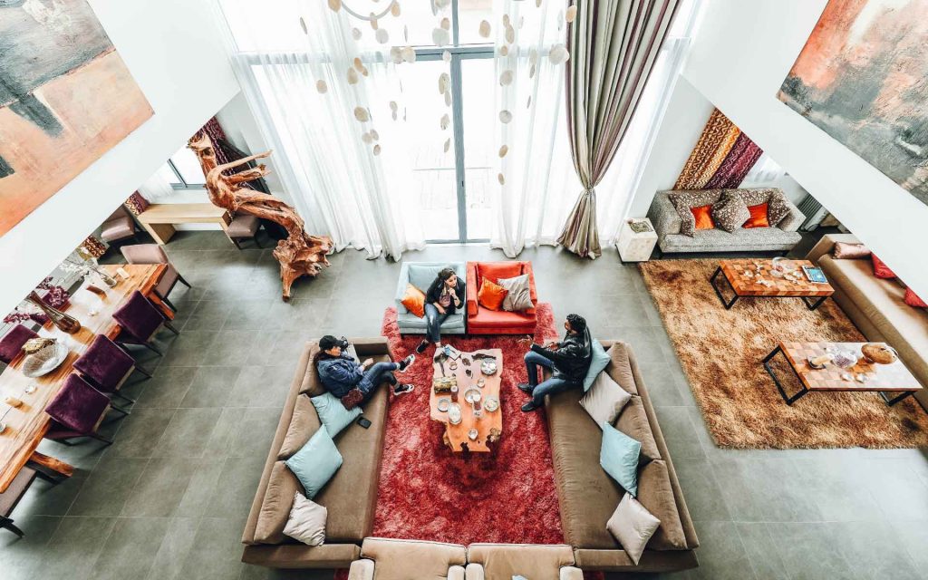 Modern living room with two people discussing over coffee, featuring a cozy layout with plush sofas, colorful cushions, and large windows allowing natural light.