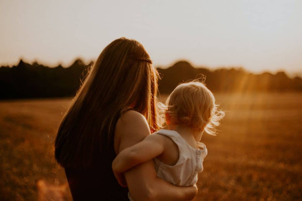 Mother holding child in a field at sunset, symbolizing family financial planning and growth.