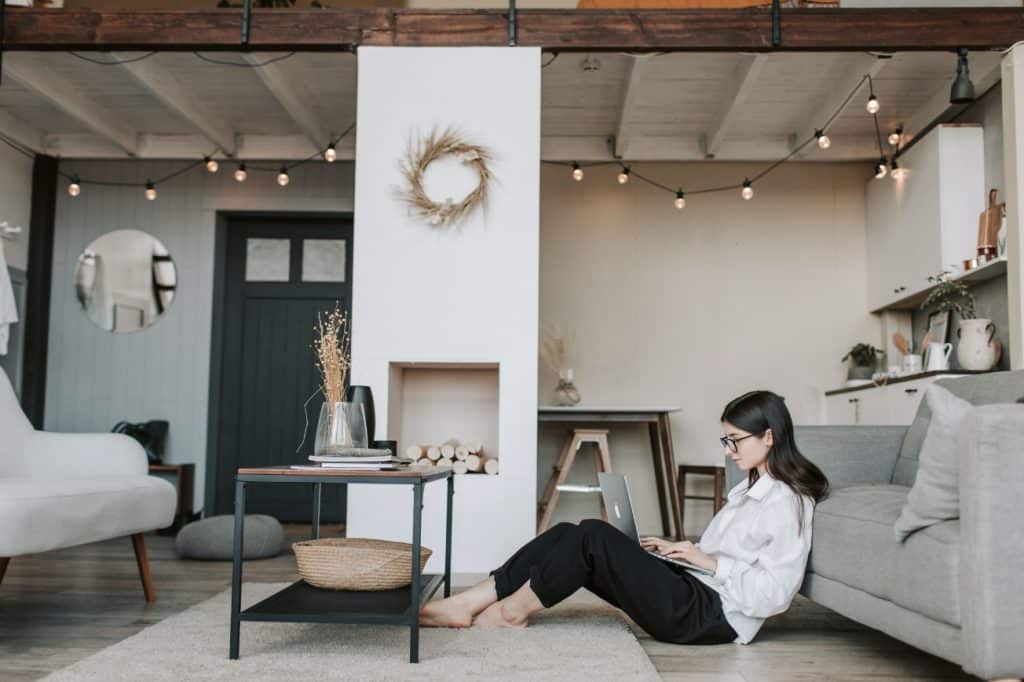 Woman working on a laptop in a cozy, modern living room with stylish decor, emphasizing productivity and financial management.