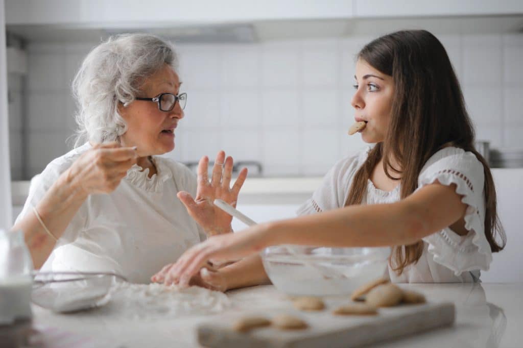 Elderly woman and young girl baking cookies together in a bright kitchen, engaging in conversation and enjoying the moment.
