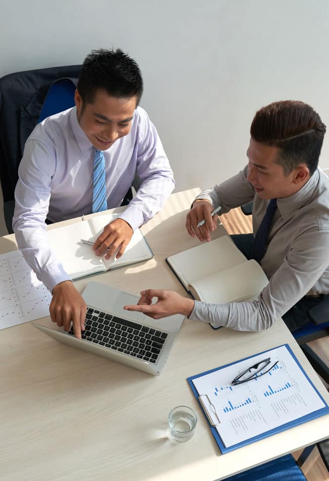 Two professionals collaborating at a desk, analyzing data on a laptop, with notebooks and financial documents, emphasizing strategic tax planning and accounting services.