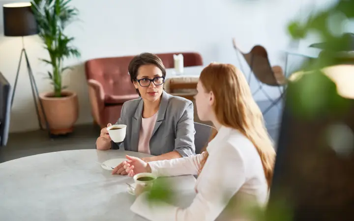 Two women engaged in a professional conversation over coffee at a modern café, representing the importance of personalized tax planning and accounting guidance.