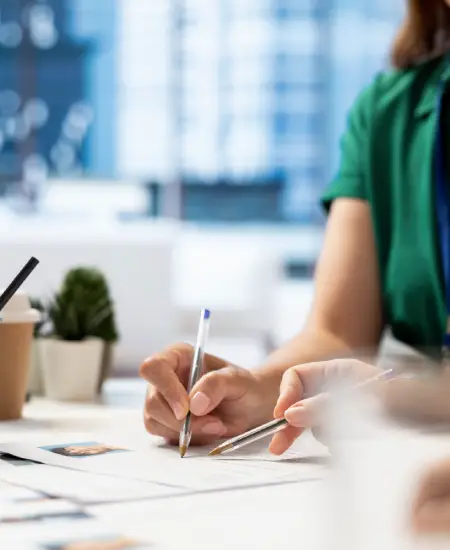 Person writing notes and reviewing documents on a table, with pens and a small plant, illustrating the attention to detail and accuracy in tax preparation and filing services.